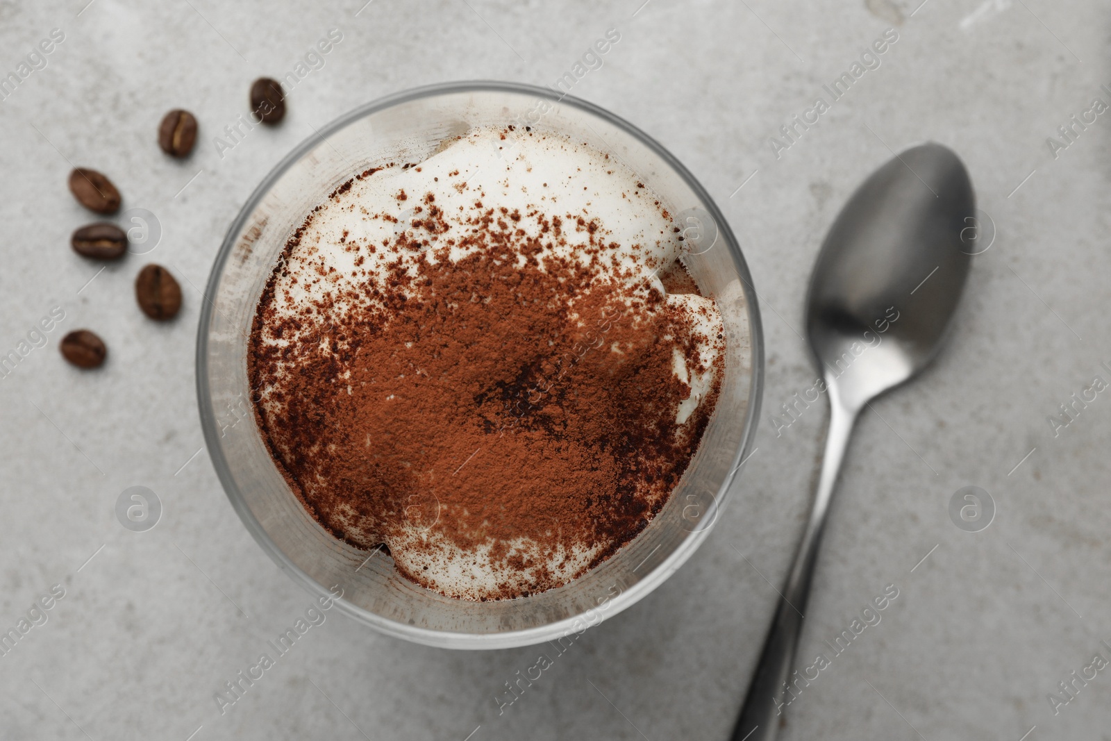 Photo of Delicious tiramisu in glass, spoon and scattered coffee beans on light table, flat lay