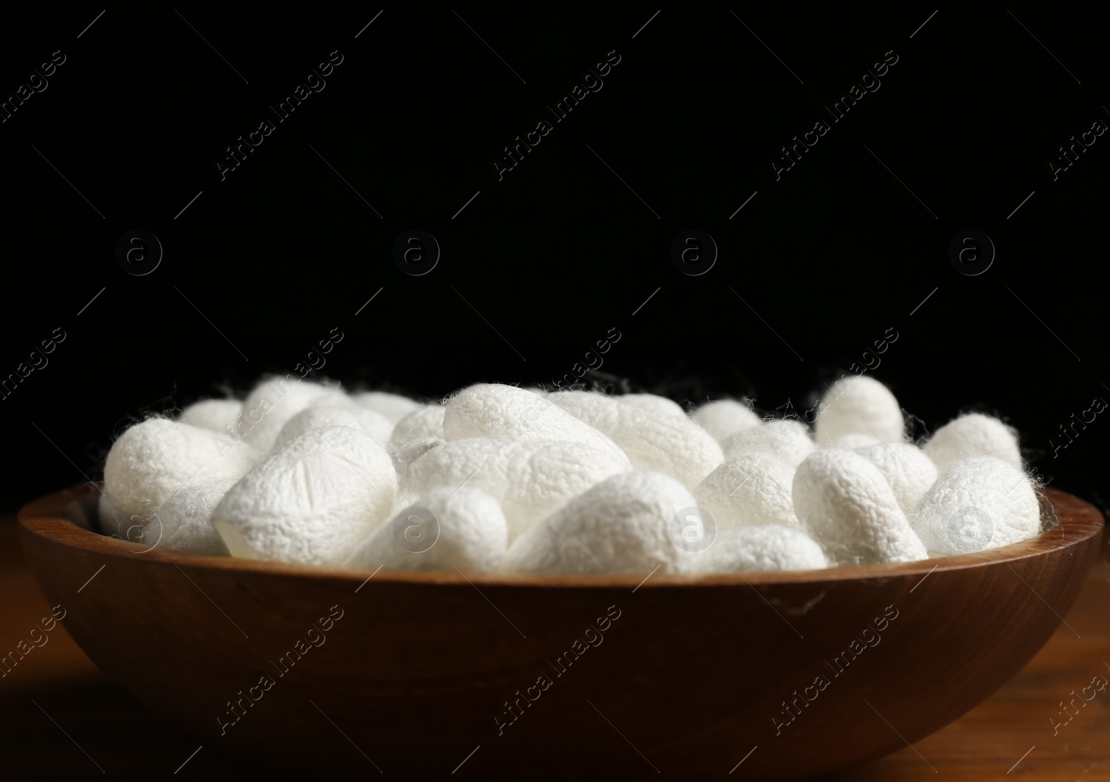 Photo of White silk cocoons in bowl on wooden table, closeup