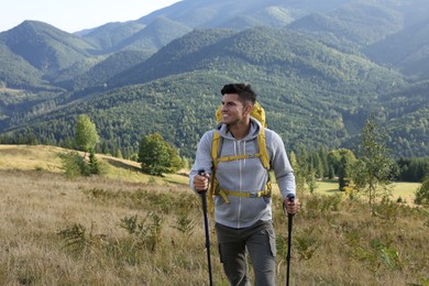 Photo of Tourist with backpack and trekking poles hiking through mountains, space for text