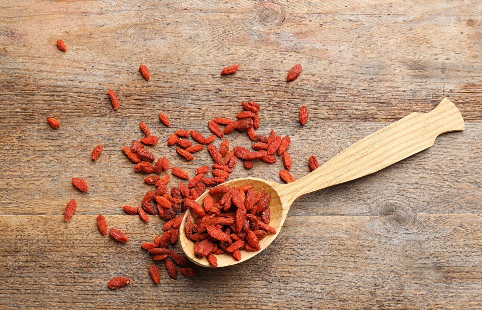 Photo of Spoon and dried goji berries on wooden table, top view. Healthy superfood