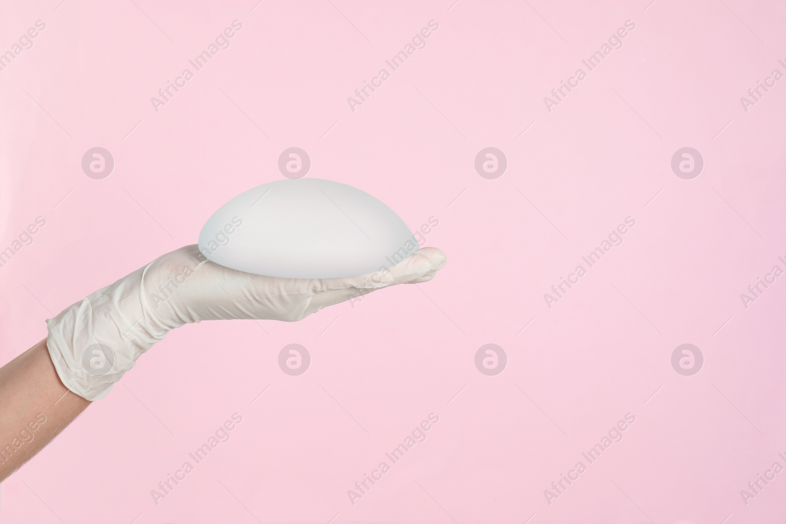 Photo of Doctor holding silicone implant for breast augmentation on color background, space for text. Cosmetic surgery