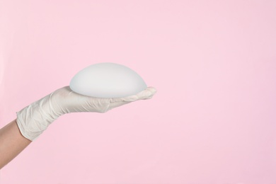 Photo of Doctor holding silicone implant for breast augmentation on color background, space for text. Cosmetic surgery