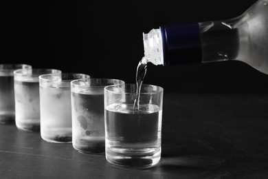 Photo of Pouring vodka from bottle in glass on grey table, closeup
