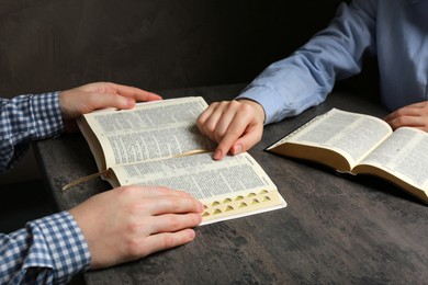 Humble couple reading Bibles at grey table together, closeup