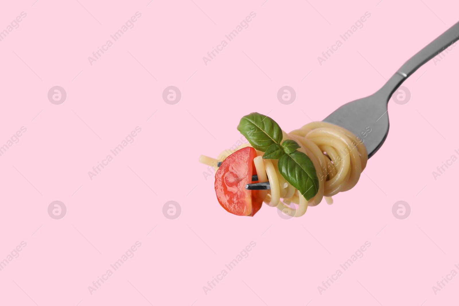 Photo of Fork with tasty pasta, piece of fresh tomato and basil on pink background, space for text