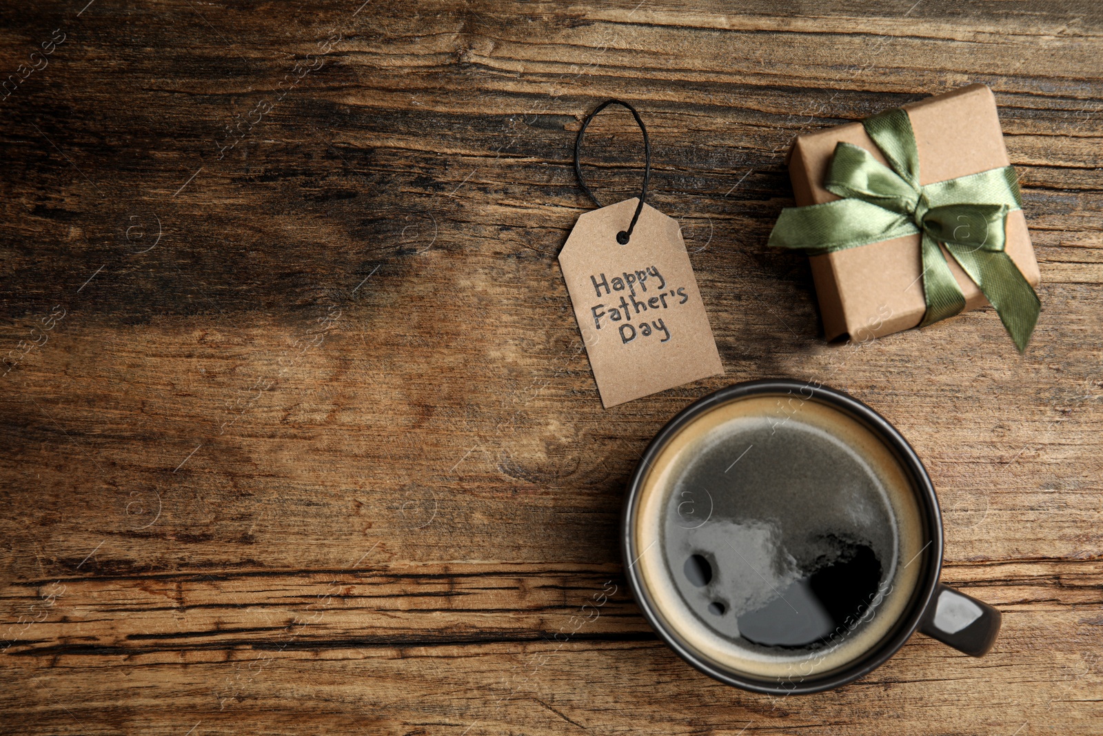 Photo of Cup of coffee, gift box and tag with phrase HAPPY FATHER'S DAY on wooden table, flat lay. Space for text