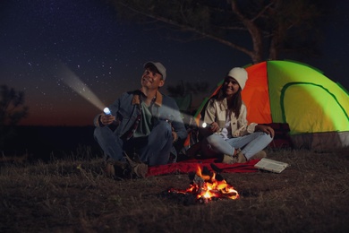 Photo of Couple with flashlights near bonfire at night. Camping season