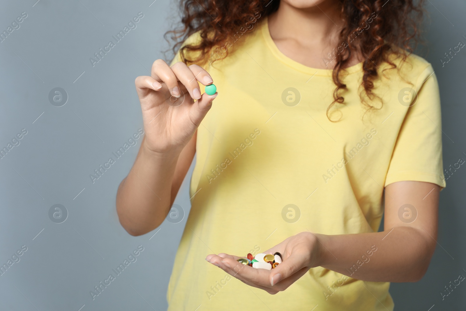 Photo of African-American woman with different vitamins on light grey background, closeup