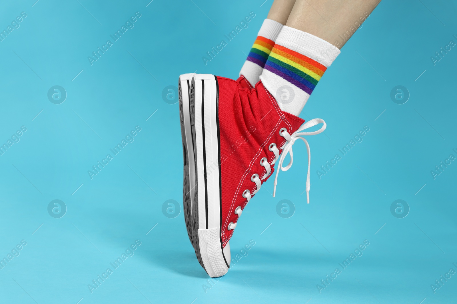 Photo of Woman in stylish gumshoes on light blue background, closeup