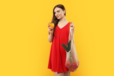 Woman with string bag of fresh vegetables on orange background