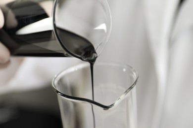 Photo of Laboratory worker pouring black crude oil into flask, closeup