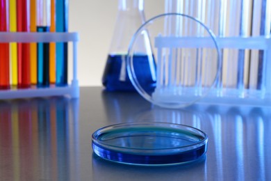 Photo of Petri dish with blue liquid on grey table in laboratory. Space for text