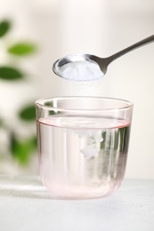 Adding baking soda into glass of water at white table against blurred background