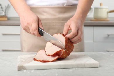 Photo of Man cutting delicious ham at grey marble table indoors, closeup