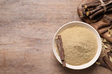 Photo of Dried sticks of liquorice root and powder on wooden table, flat lay. Space for text