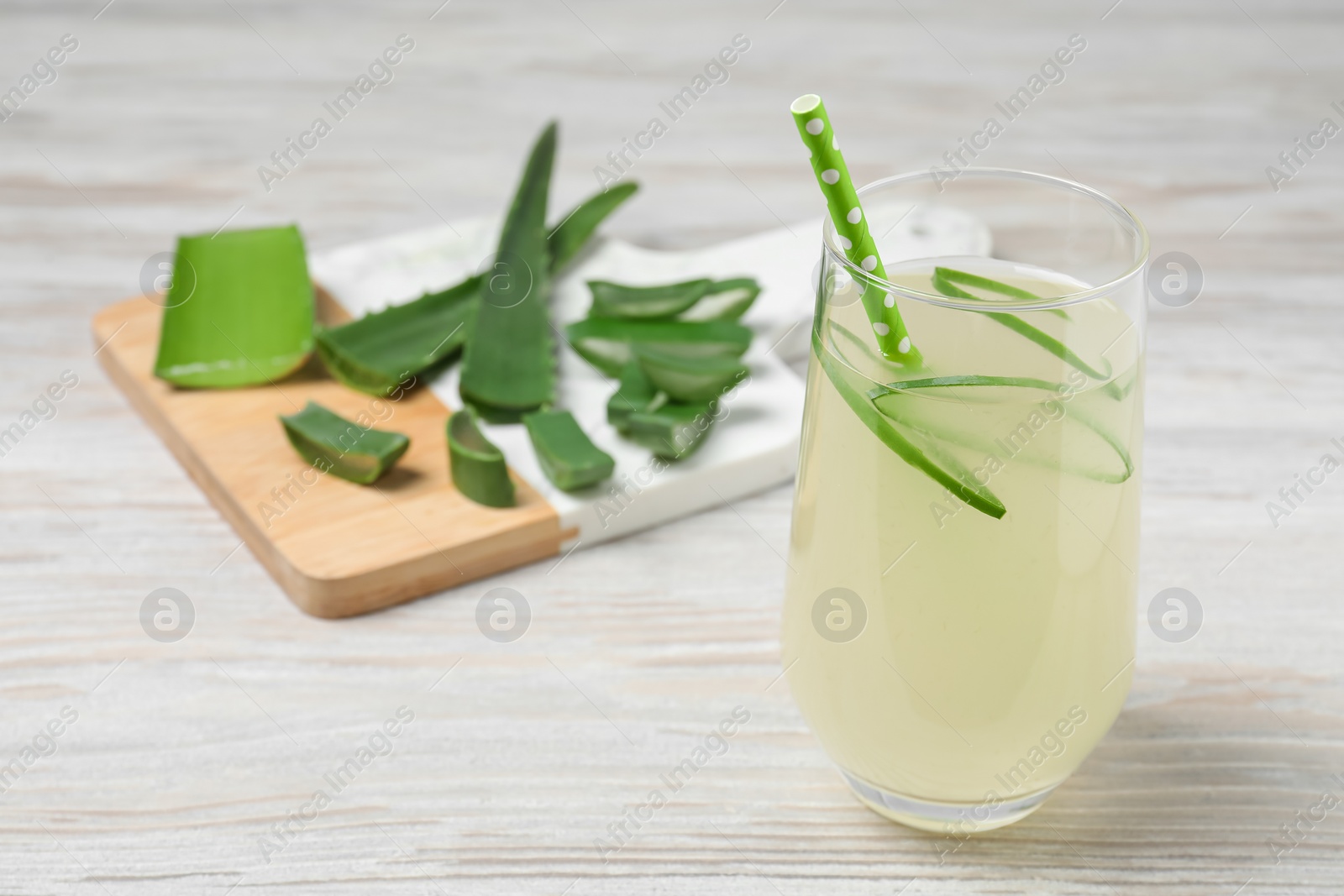 Photo of Tasty aloe juice in glass and cut fresh leaves on light wooden table