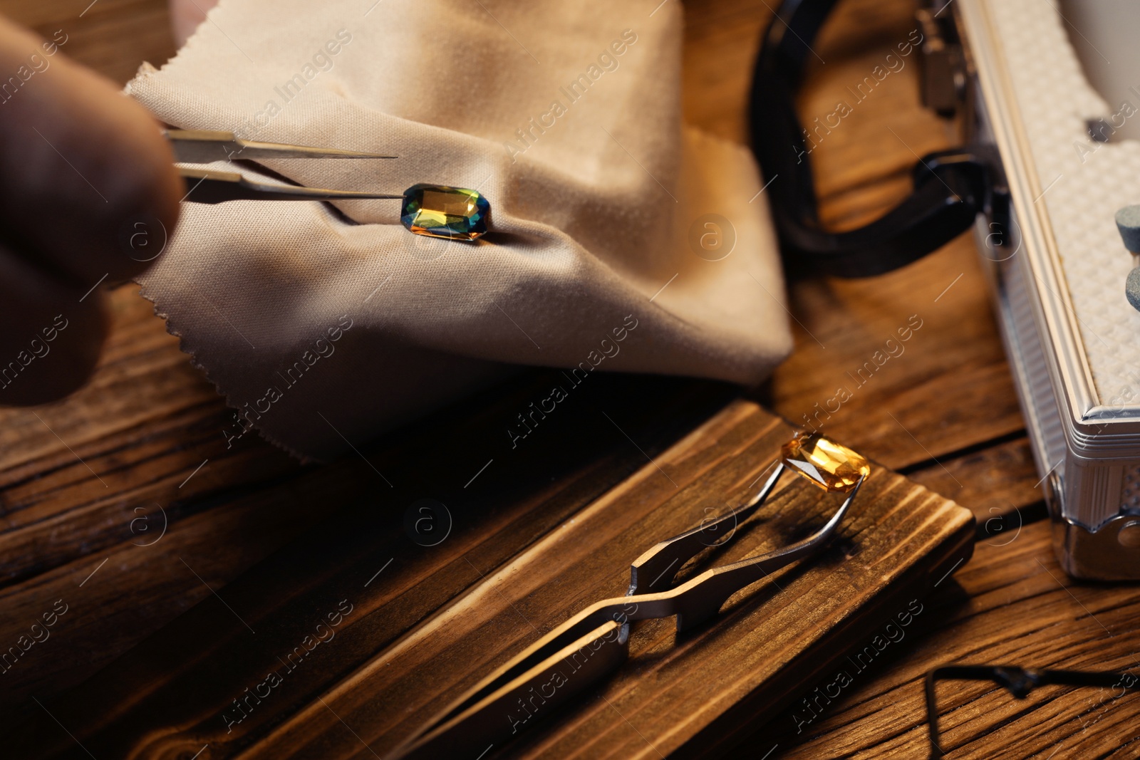 Photo of Professional jeweler working with gemstone at wooden table, closeup
