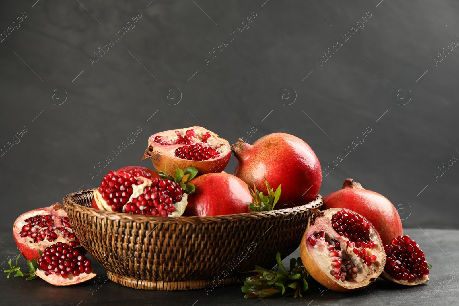 Photo of Delicious ripe pomegranates in bowl on black table