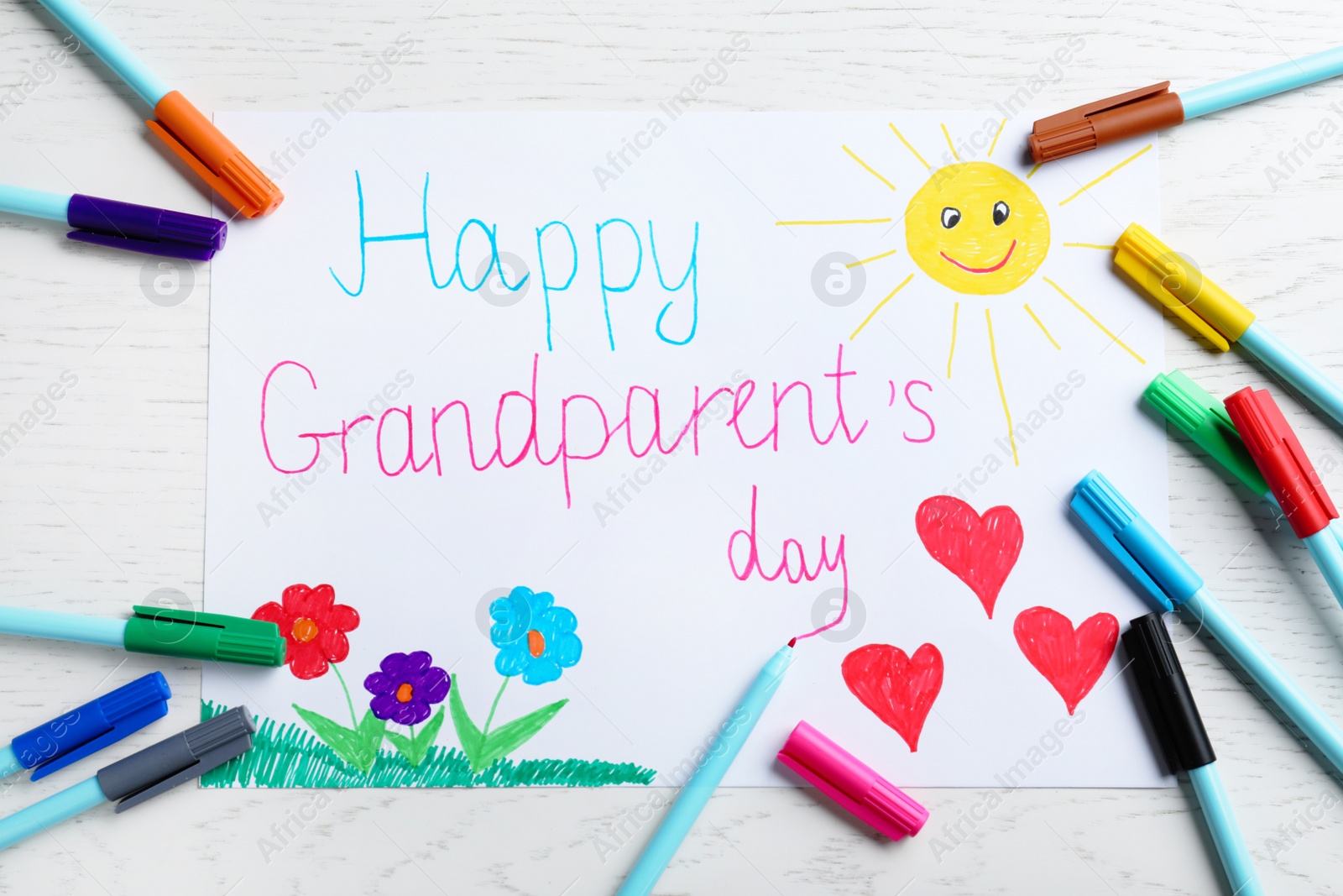 Photo of Beautiful drawing with phrase Happy Grandparents Day on white wooden table, flat lay