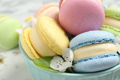 Delicious colorful macarons and flowers in bowl on table, closeup