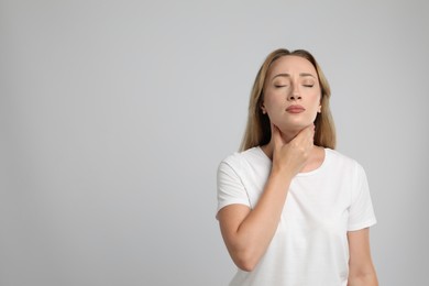 Photo of Young woman doing thyroid self examination on light grey background, space for text