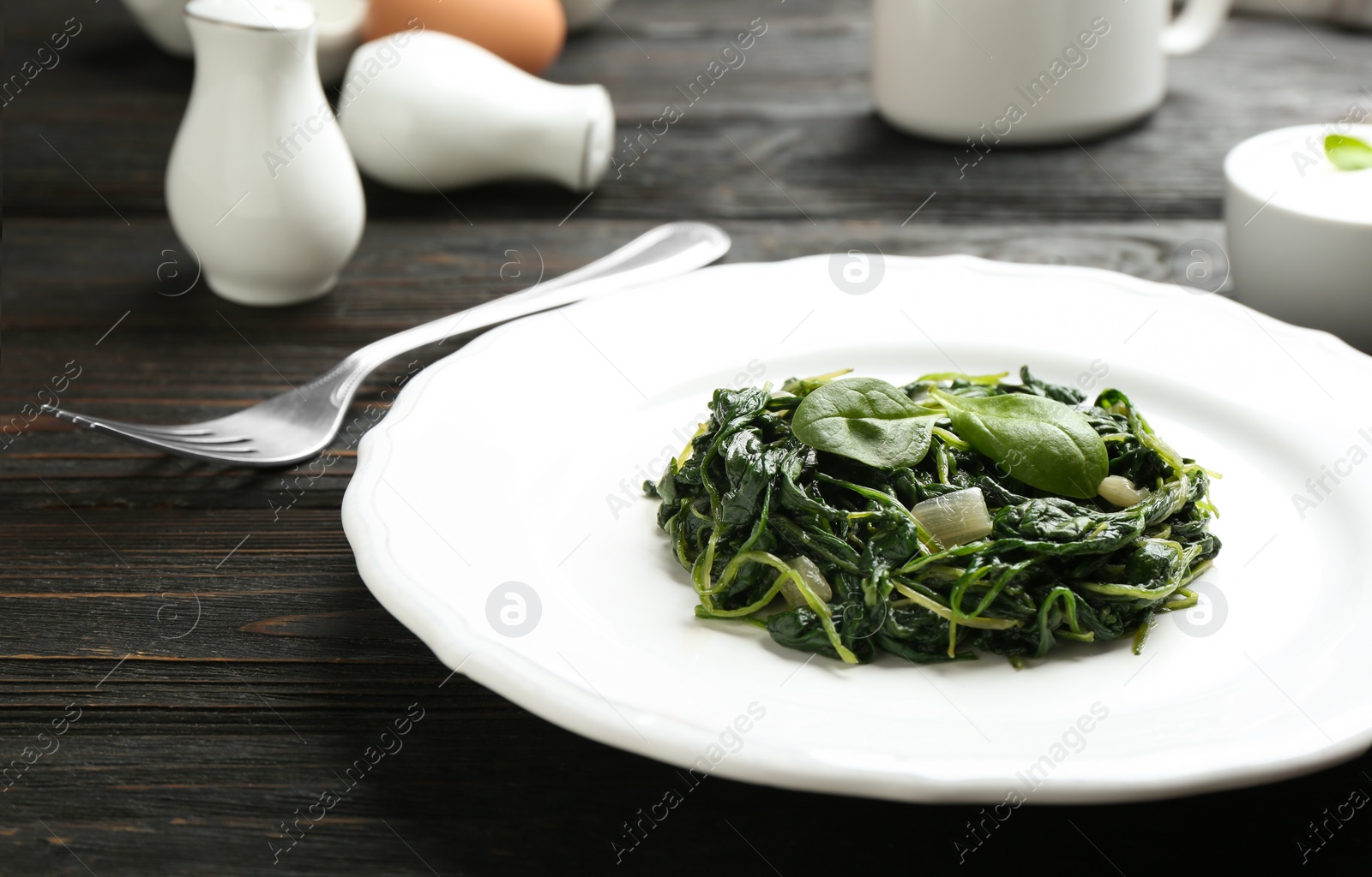 Photo of Plate with tasty cooked spinach on black wooden table, closeup. Healthy food