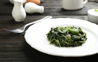 Photo of Plate with tasty cooked spinach on black wooden table, closeup. Healthy food