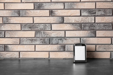 Napkin holder with paper serviettes on table against brick wall. Space for text