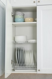 Clean plates and bowls on shelves in cabinet indoors