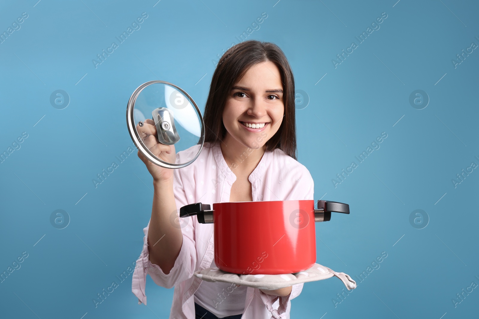 Photo of Happy young woman with cooking pot on light blue background