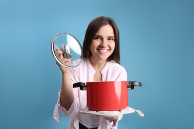 Happy young woman with cooking pot on light blue background