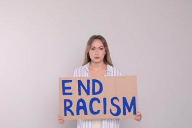 Photo of Young woman holding sign with phrase End Racism on light background