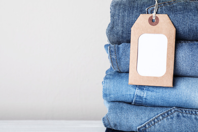 Photo of Stack of different jeans with tag on light background, closeup. Space for text