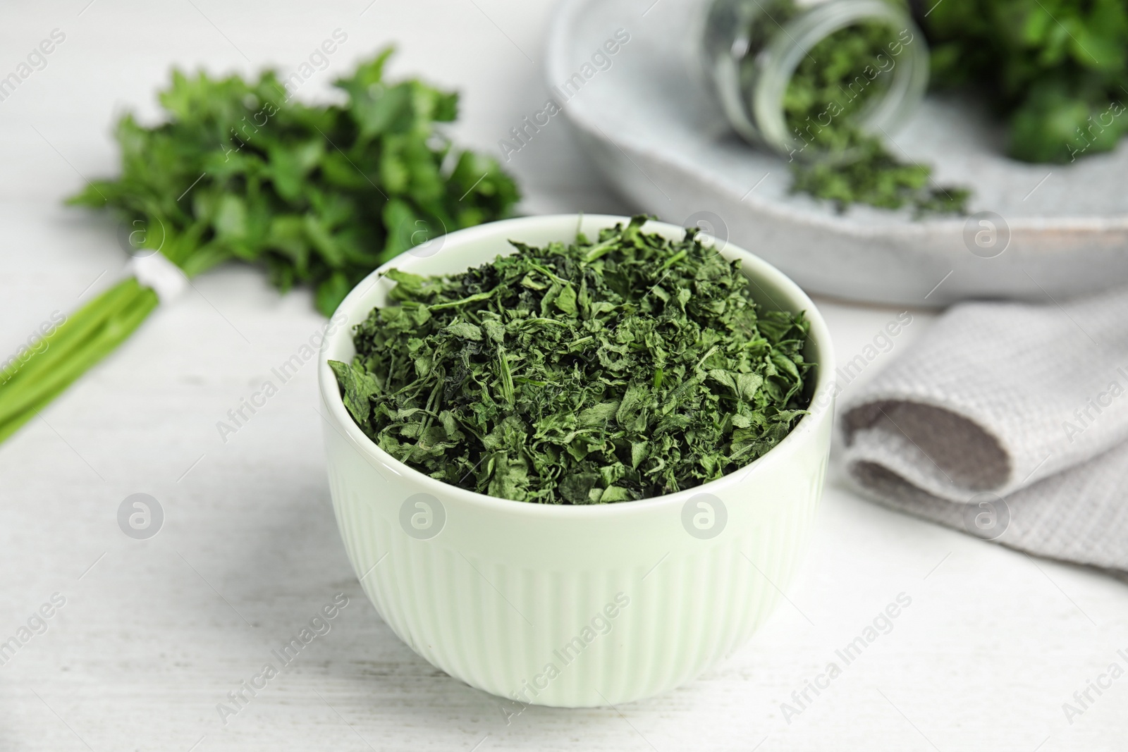Photo of Bowl with dried parsley on white wooden table