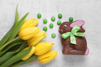 Flat lay composition with chocolate Easter bunny, beautiful tulips and candies on white textured table