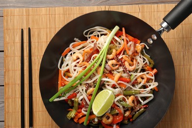 Shrimp stir fry with noodles and vegetables in wok on wooden table, top view