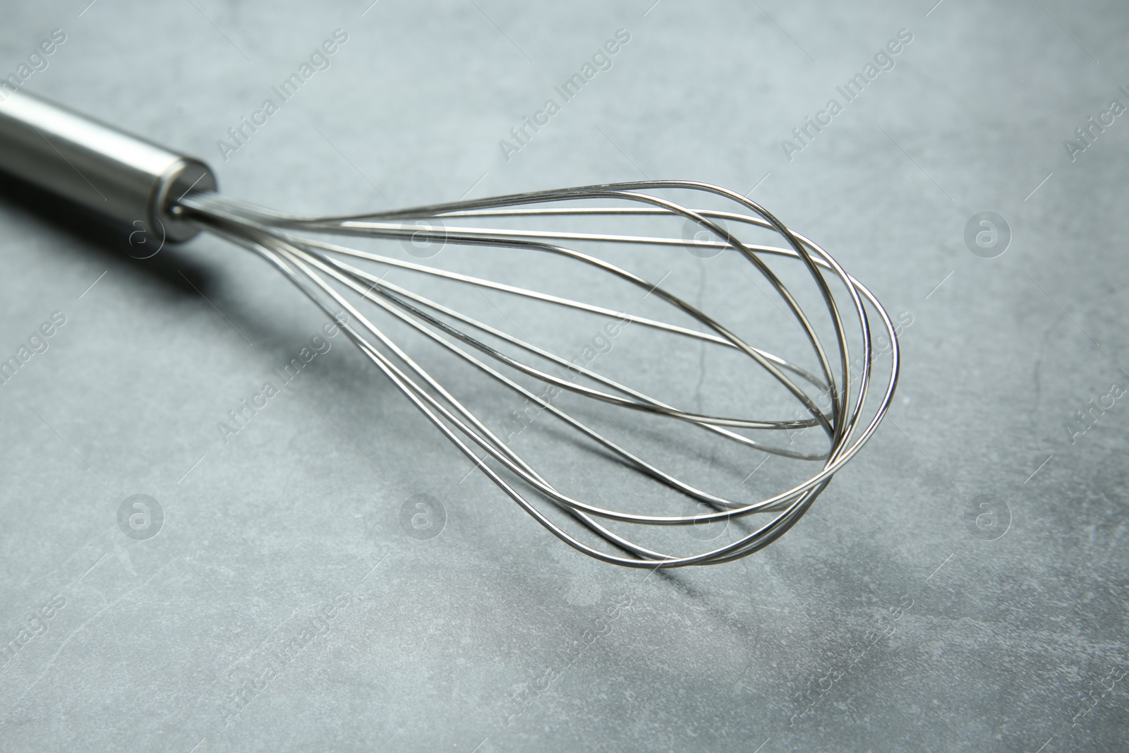 Photo of Metal whisk on gray table, closeup. Kitchen tool