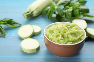 Bowl with green tasty puree, zucchini and basil on light blue wooden table, closeup