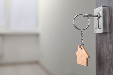 Photo of Mortgage and real estate. Open door with key and house shaped keychain against blurred background, space for text