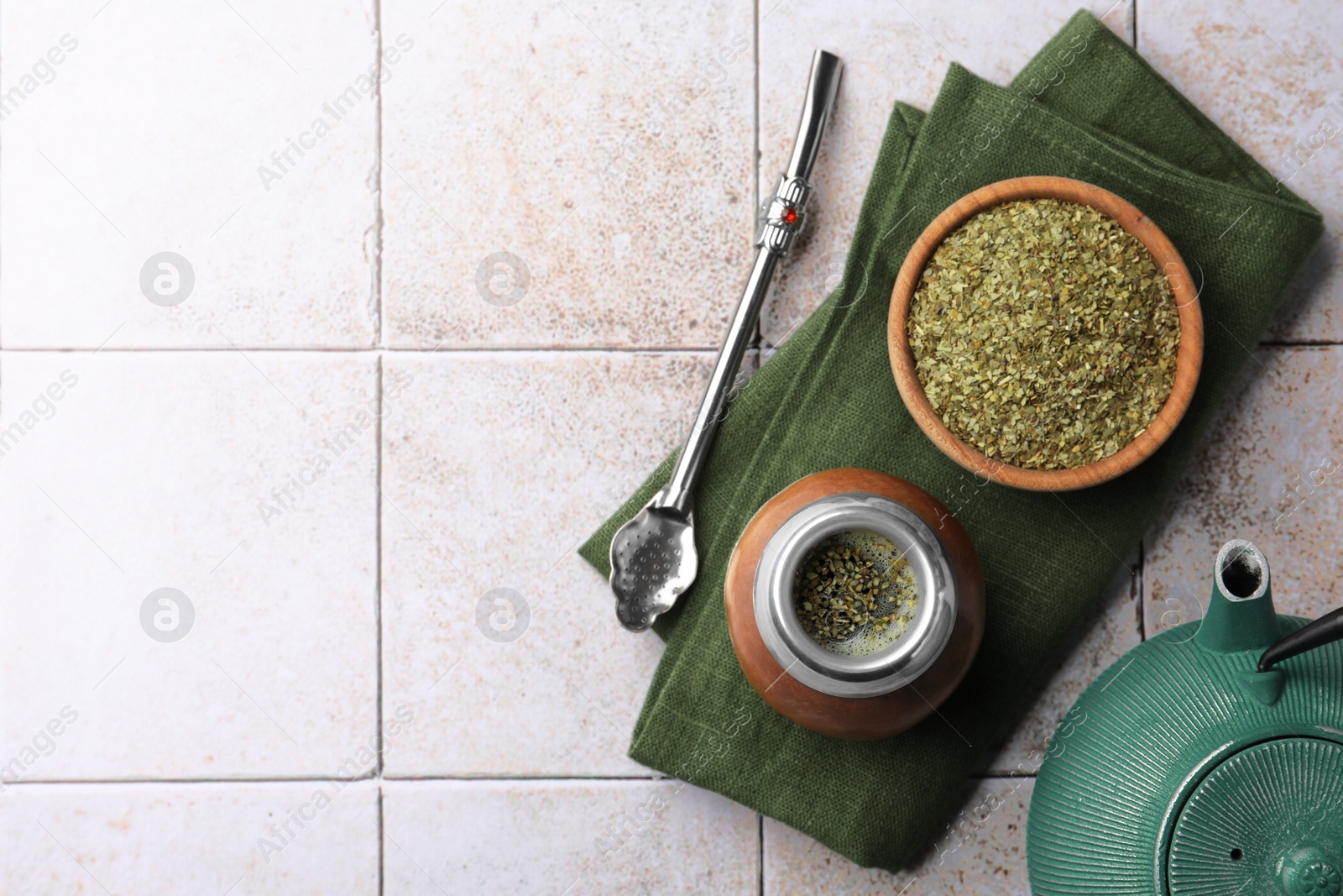 Photo of Calabash, bombilla, bowl of mate tea leaves and teapot on tiled table, flat lay. Space for text