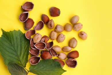 Photo of Tasty organic hazelnuts and leaves on yellow background, flat lay