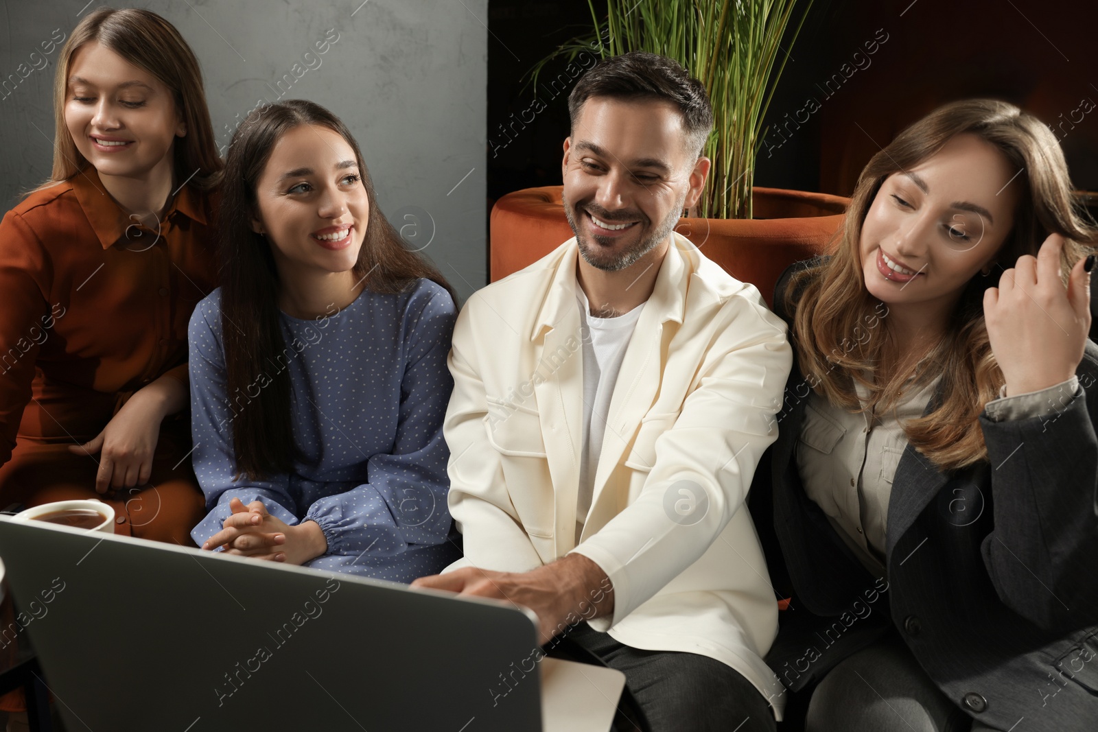 Photo of Young women and man with laptop spending time together in cafe