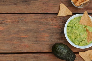 Delicious guacamole, avocado and nachos on wooden table, flat lay. Space for text