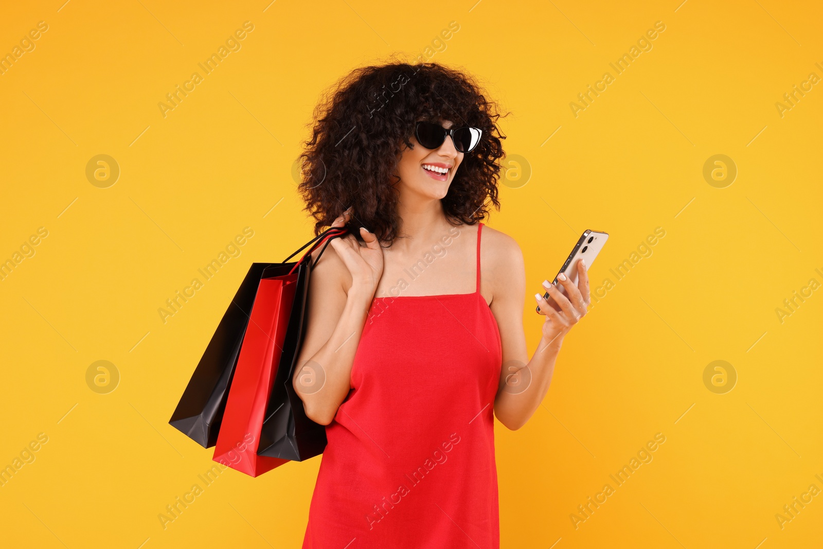 Photo of Happy young woman with shopping bags and modern smartphone on yellow background