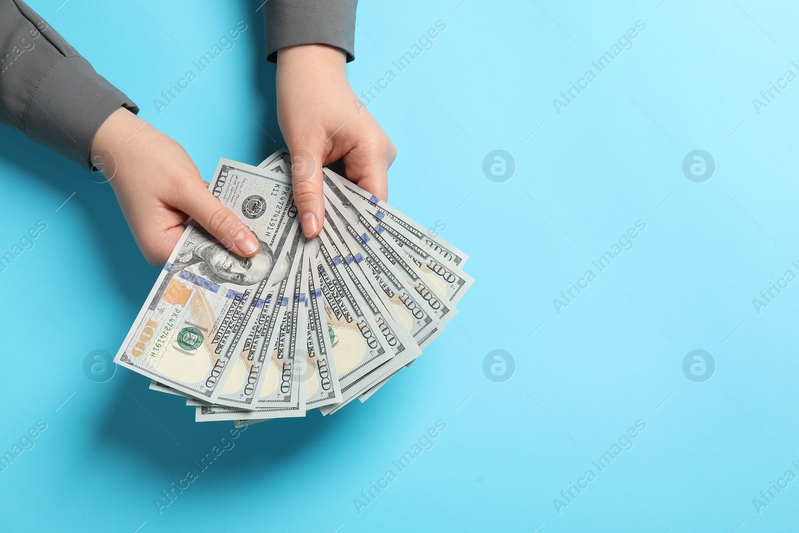 Photo of Money exchange. Woman holding dollar banknotes on light blue background, top view. Space for text