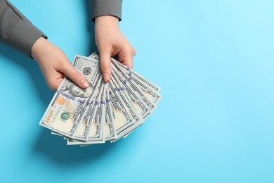 Photo of Money exchange. Woman holding dollar banknotes on light blue background, top view. Space for text