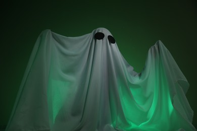 Photo of Creepy ghost. Woman covered with sheet in green light, low angle view