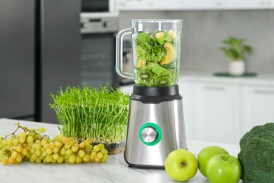 Photo of Blender with ingredients for smoothie and products on white marble table in kitchen