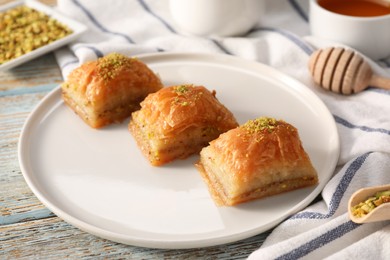 Photo of Delicious sweet baklava with pistachios on light blue wooden table, closeup