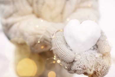 Photo of Woman holding Christmas lights and heart made of snow, closeup